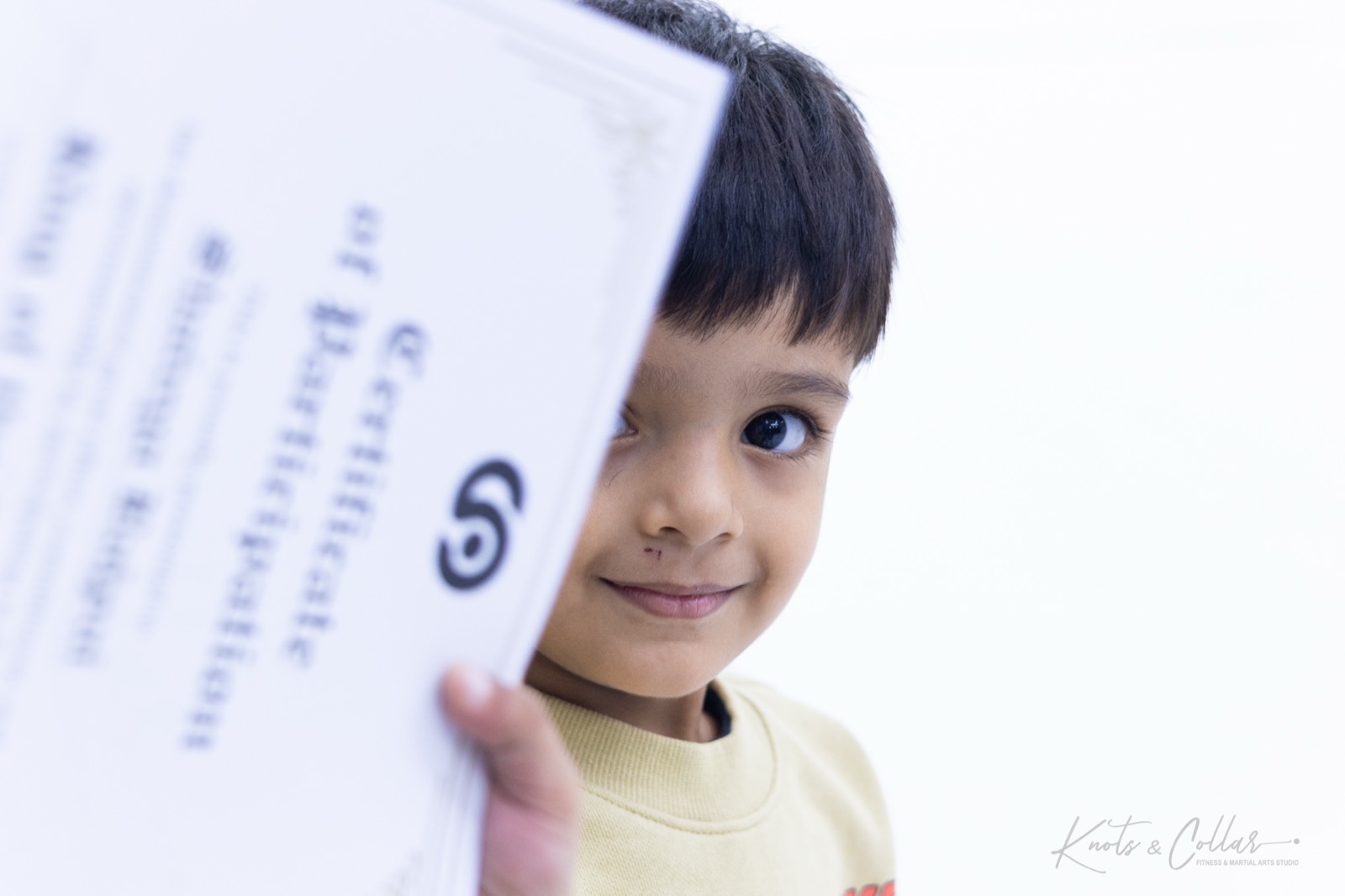 A young competitor holding up his certificate of participation from a kids BJJ tournament